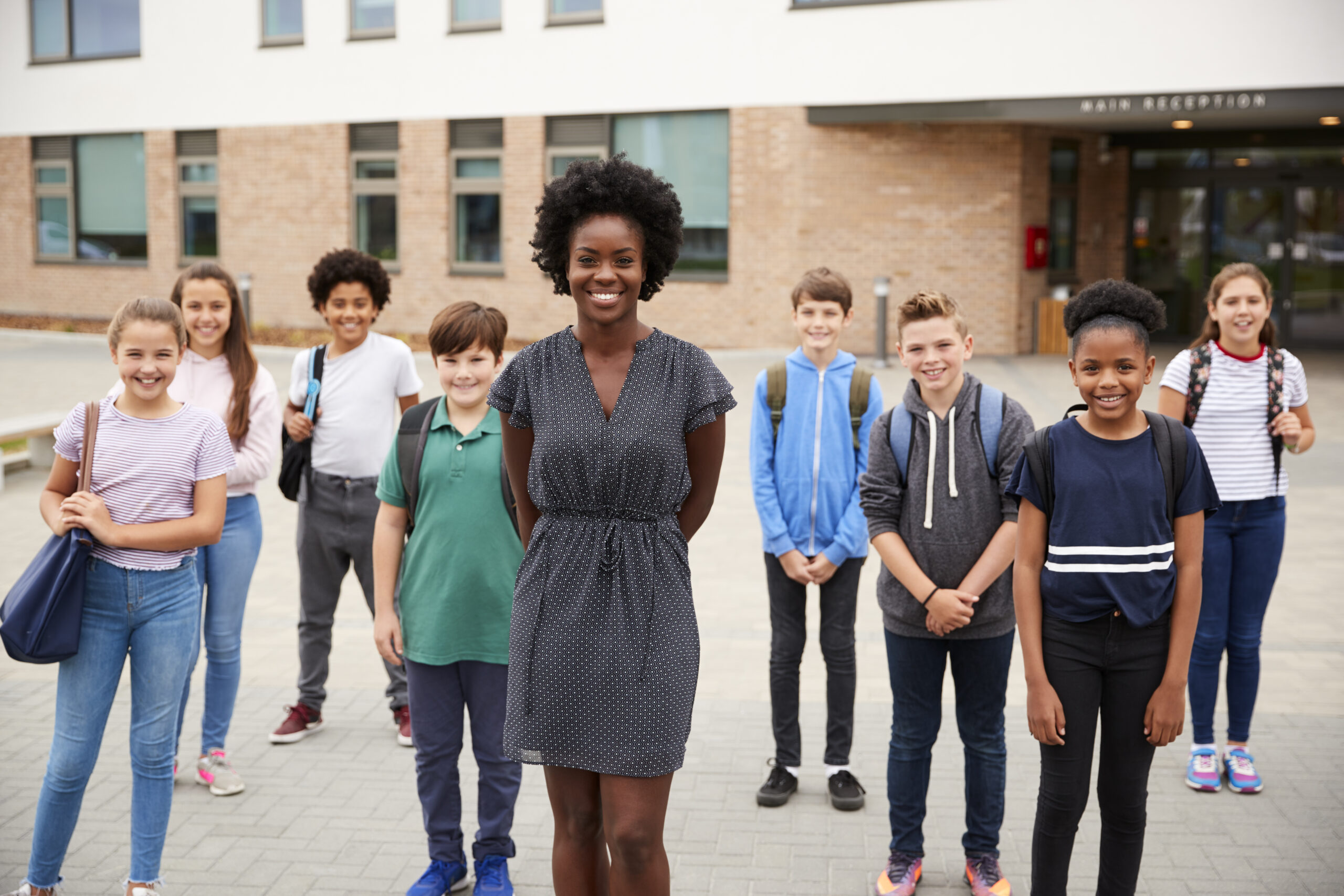pexels-rodnae-productions-7414041 A group of young people with backpacks stand outside a building with large windows, accompanied by an adult in a dark dress.
