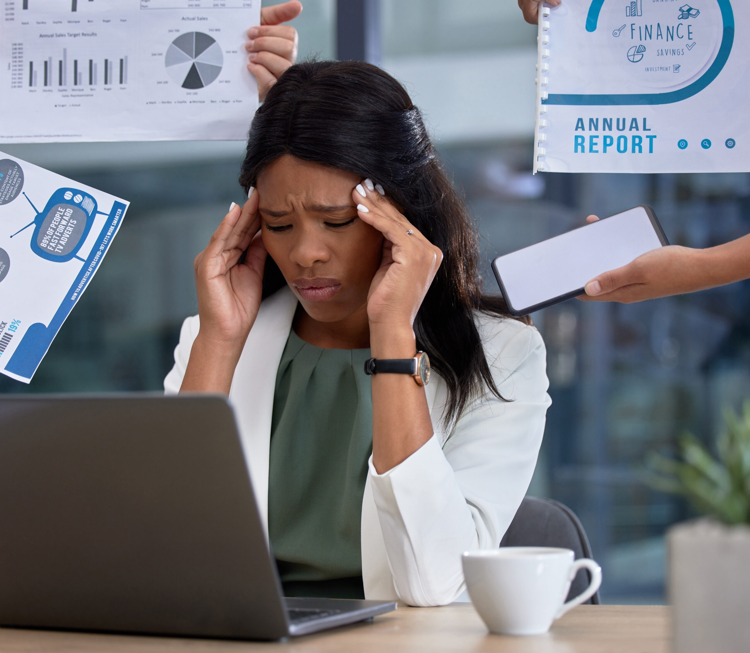 A person sits at a desk with a laptop, surrounded by documents held by others, suggesting workplace pressure or information overload.