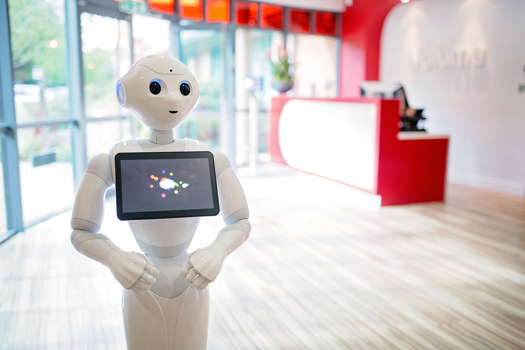 Humanoid robot in a modern office reception area with tablet interface