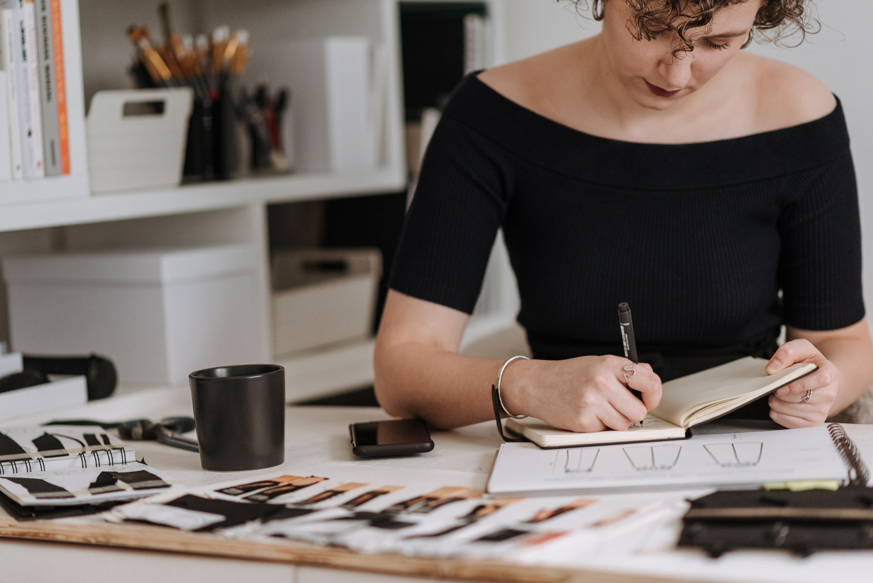 "Person sketching in a creative workspace filled with art supplies and books"