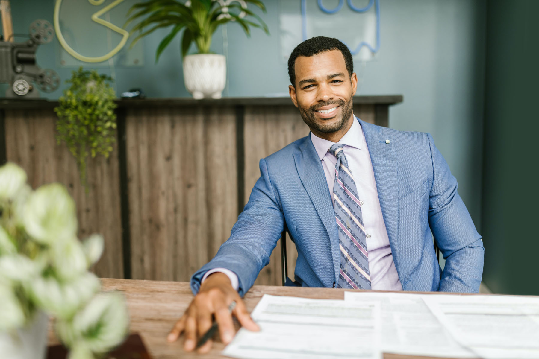 Person in a blue suit seated at a desk with papers in a professional office setting.