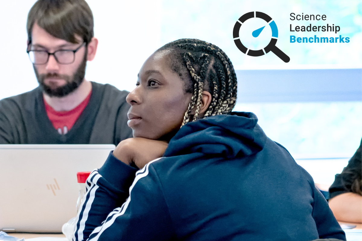 Two educators in a classroom setting, one working on a laptop, with a visible "Science Leadership Benchmarks" logo on the wall.