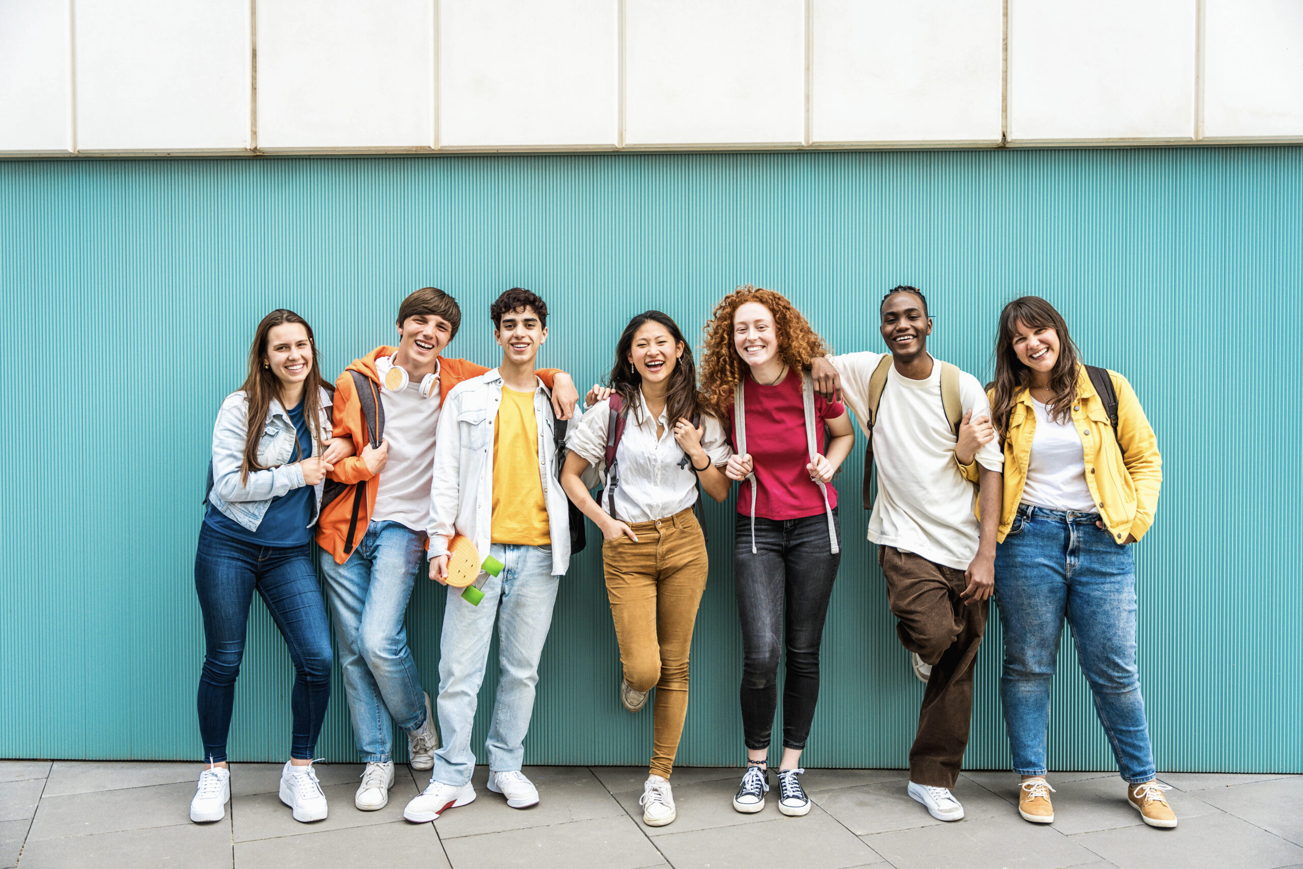 diverse college students standing together in front of a cyan coloured wall.