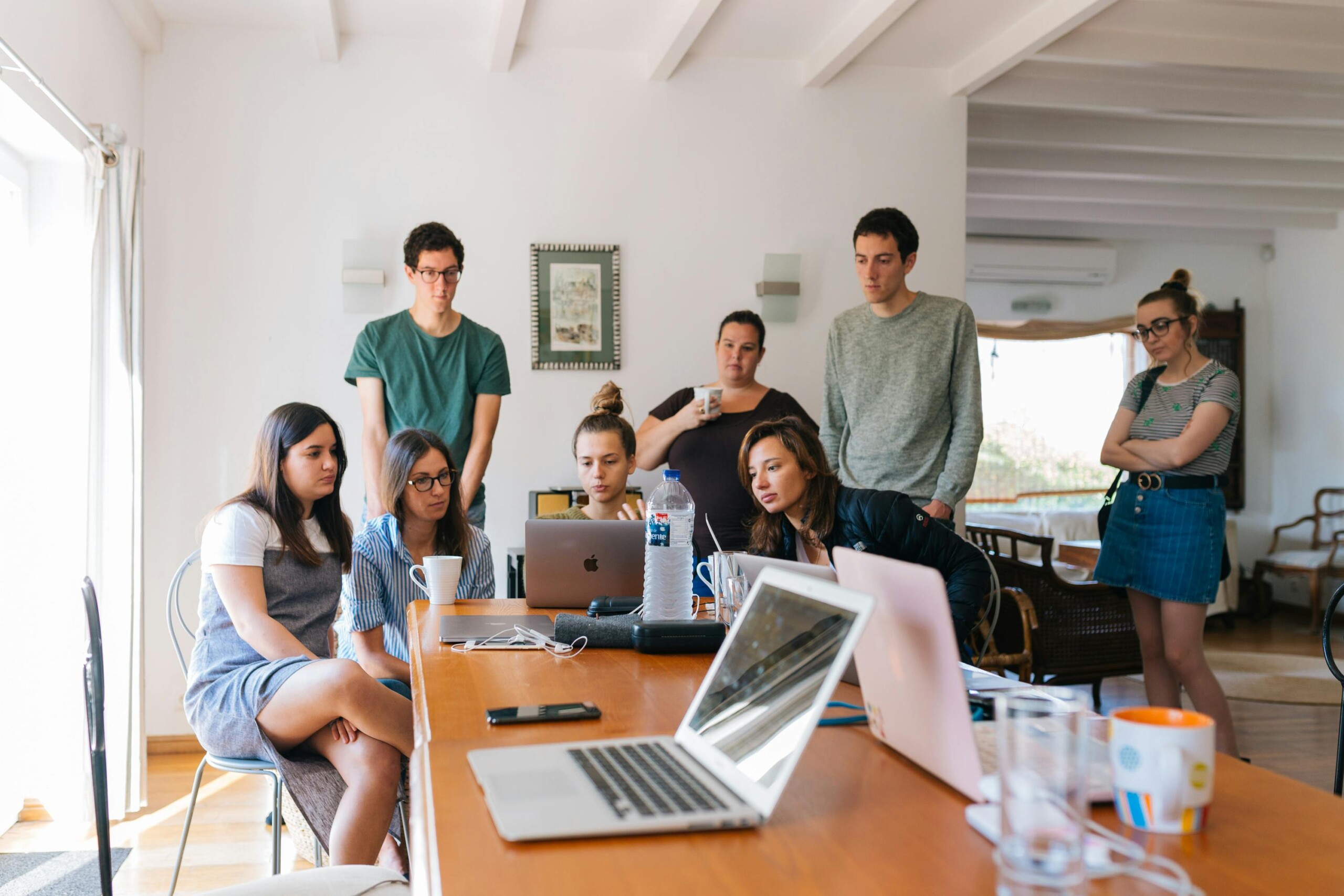 Group of people collaborating around a table with laptops in an indoor setting.