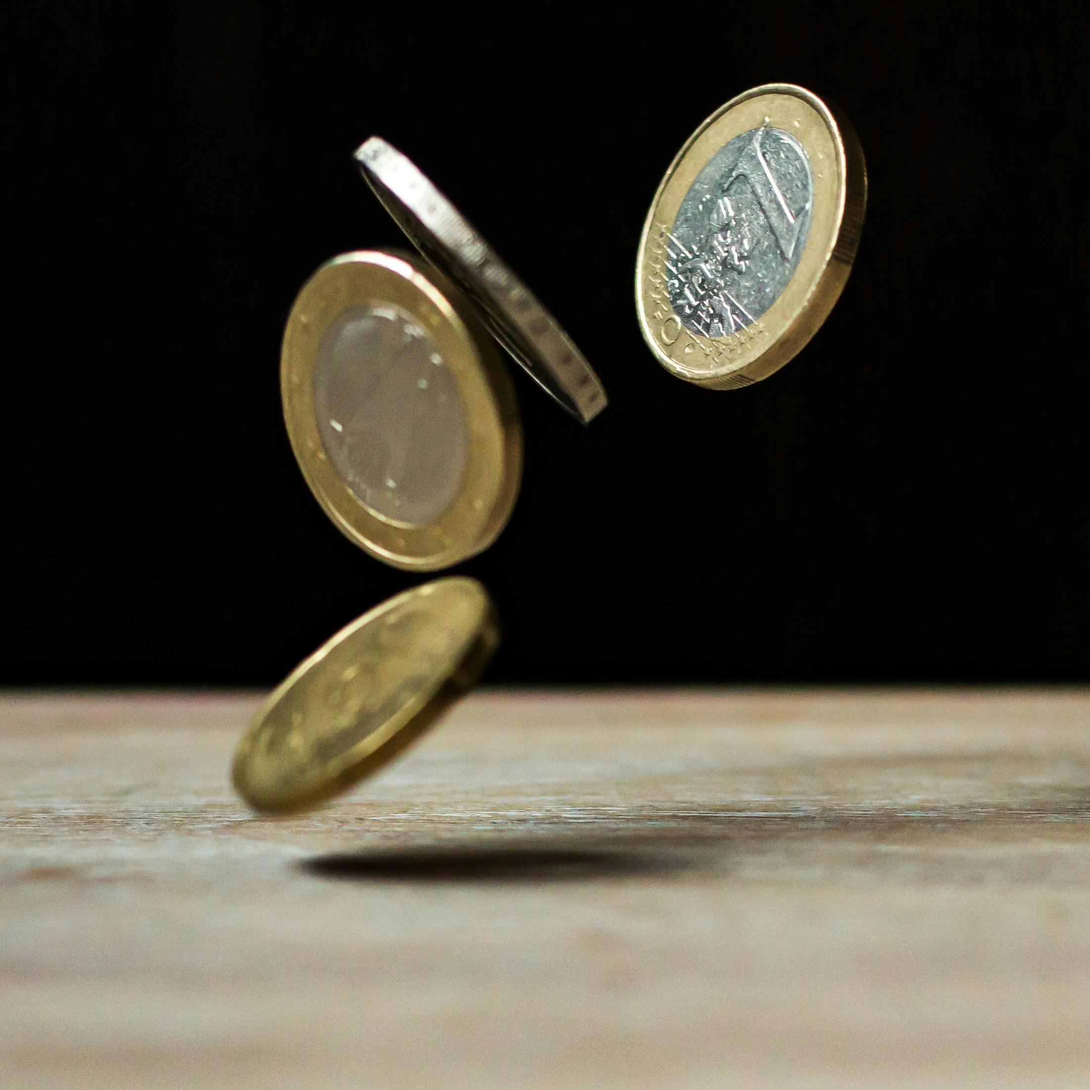 Four Euro coins flipping in mid-air over a wooden surface