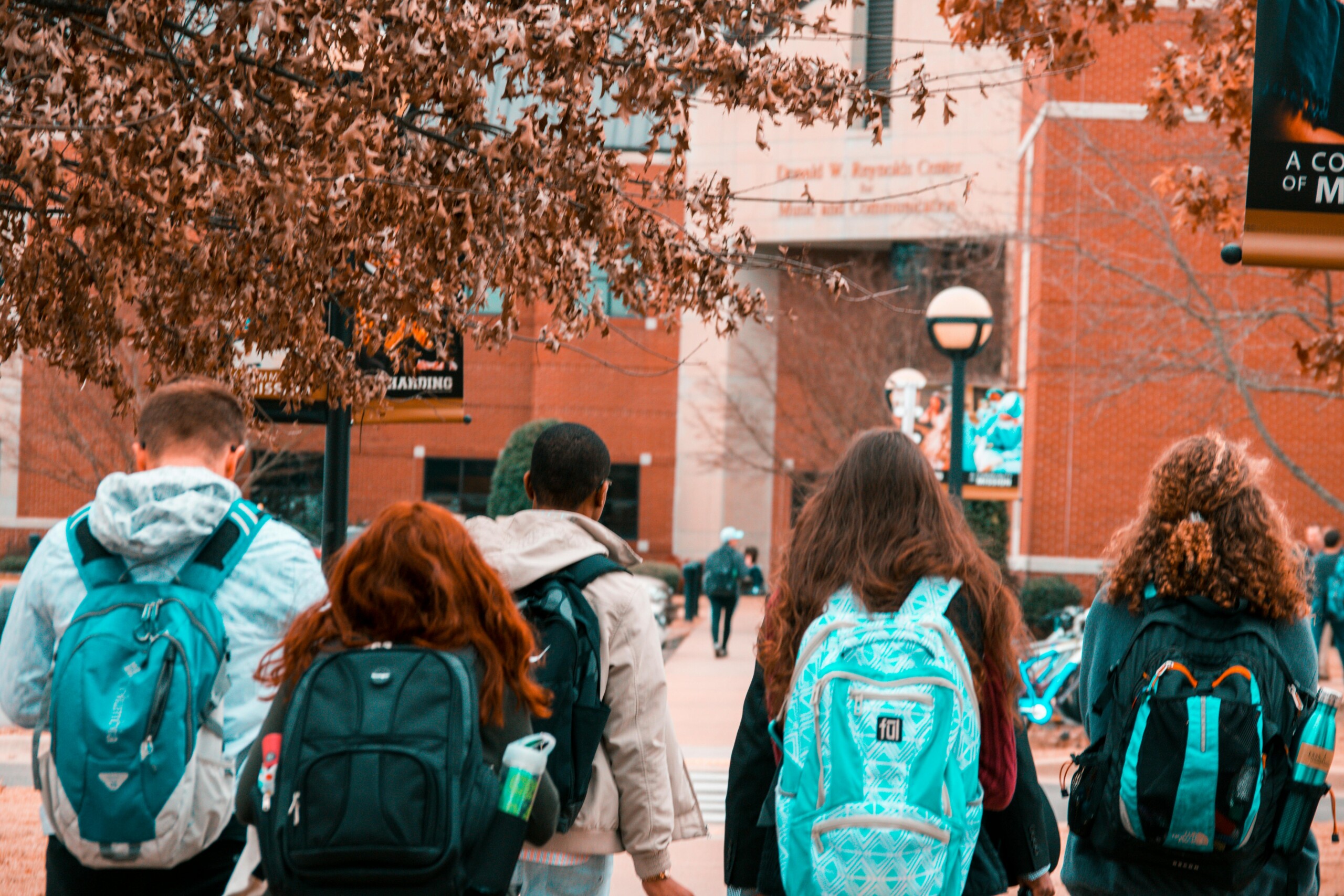 Students walking towards a university building with backpacks on a sunny day