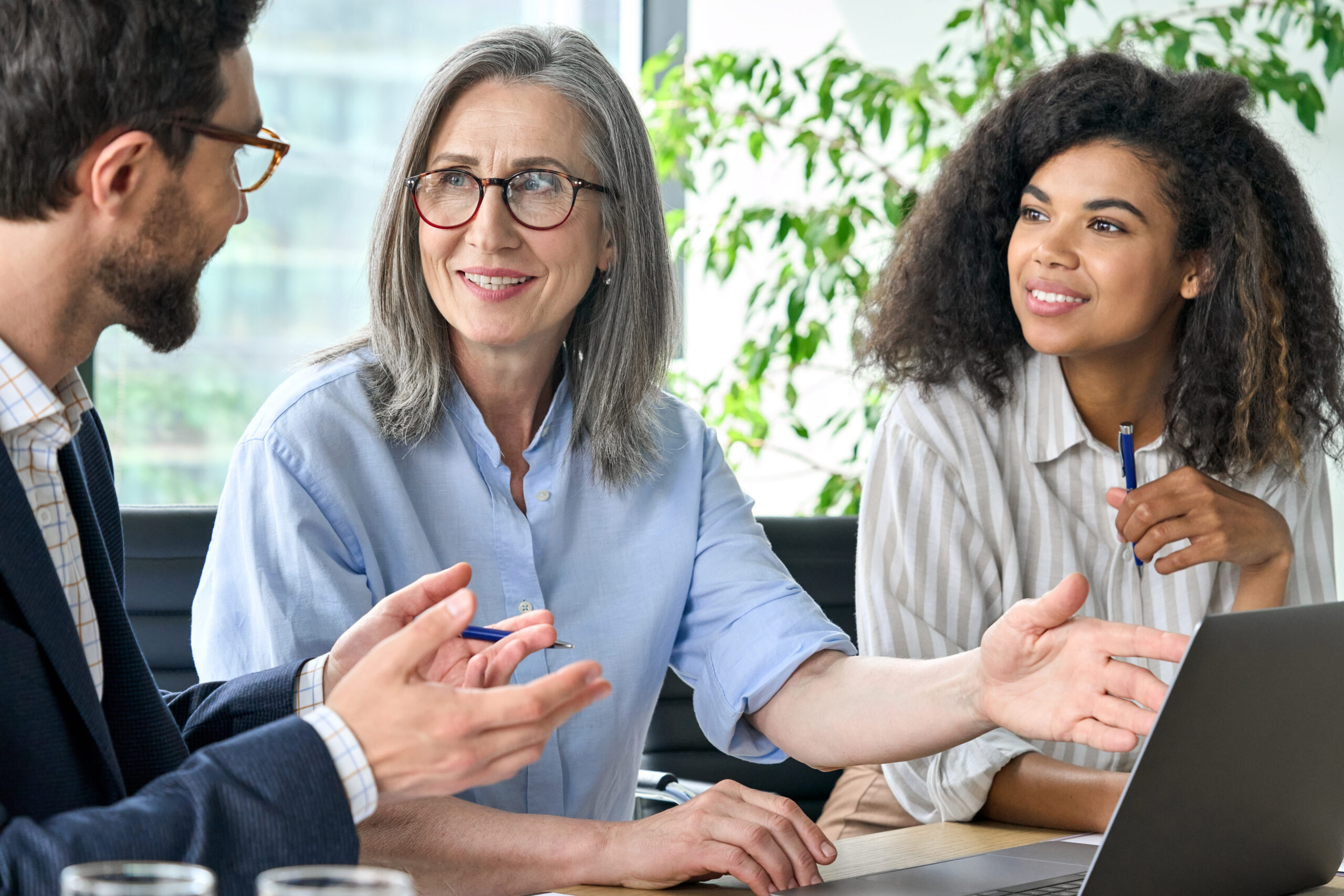 A diverse trio of business people in a modern office setting with plants discussing the Skills and Business hub