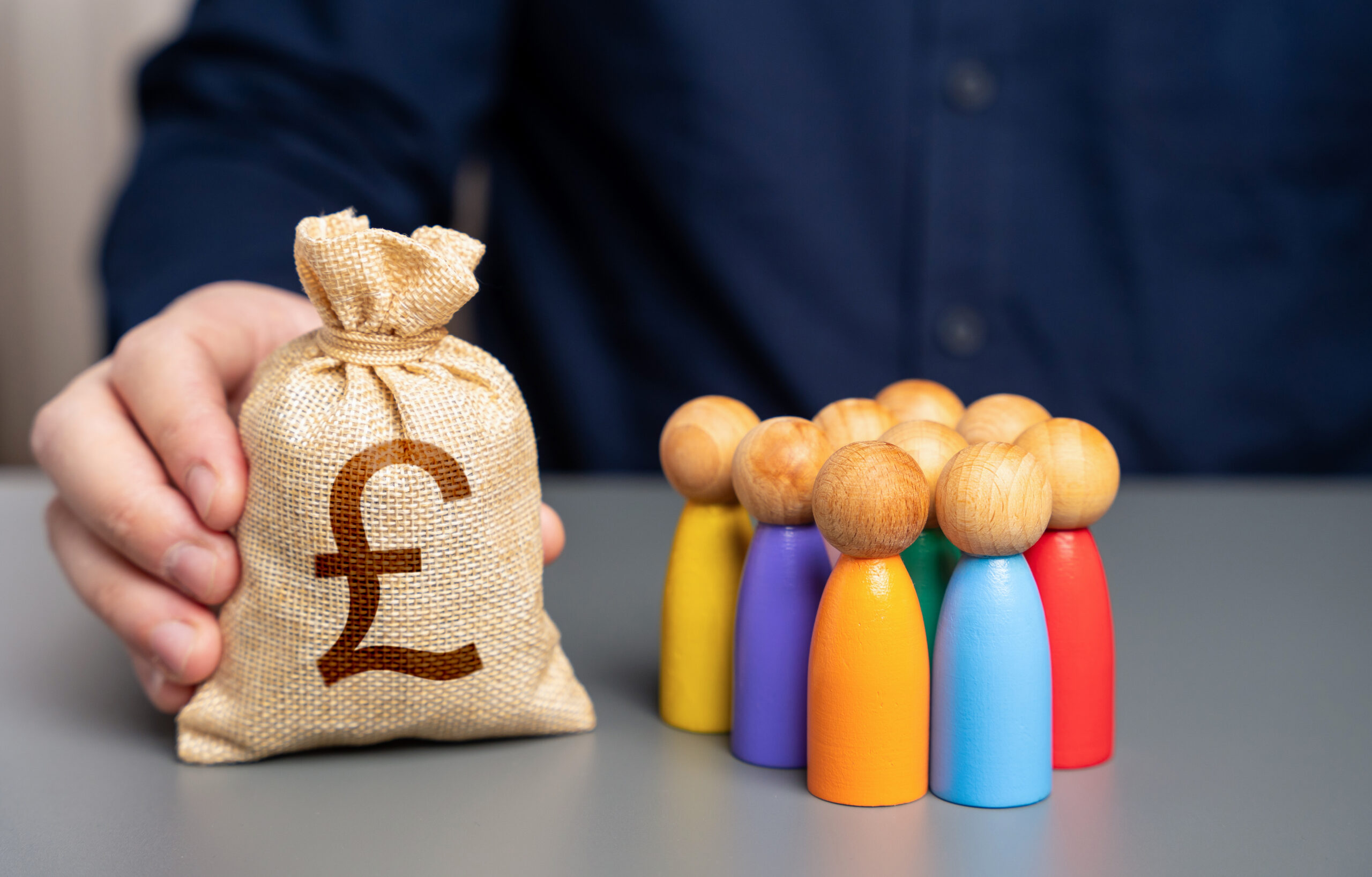 funding for growth. A businessman holds a british pound sterling money bag next to wooden figurines of people.