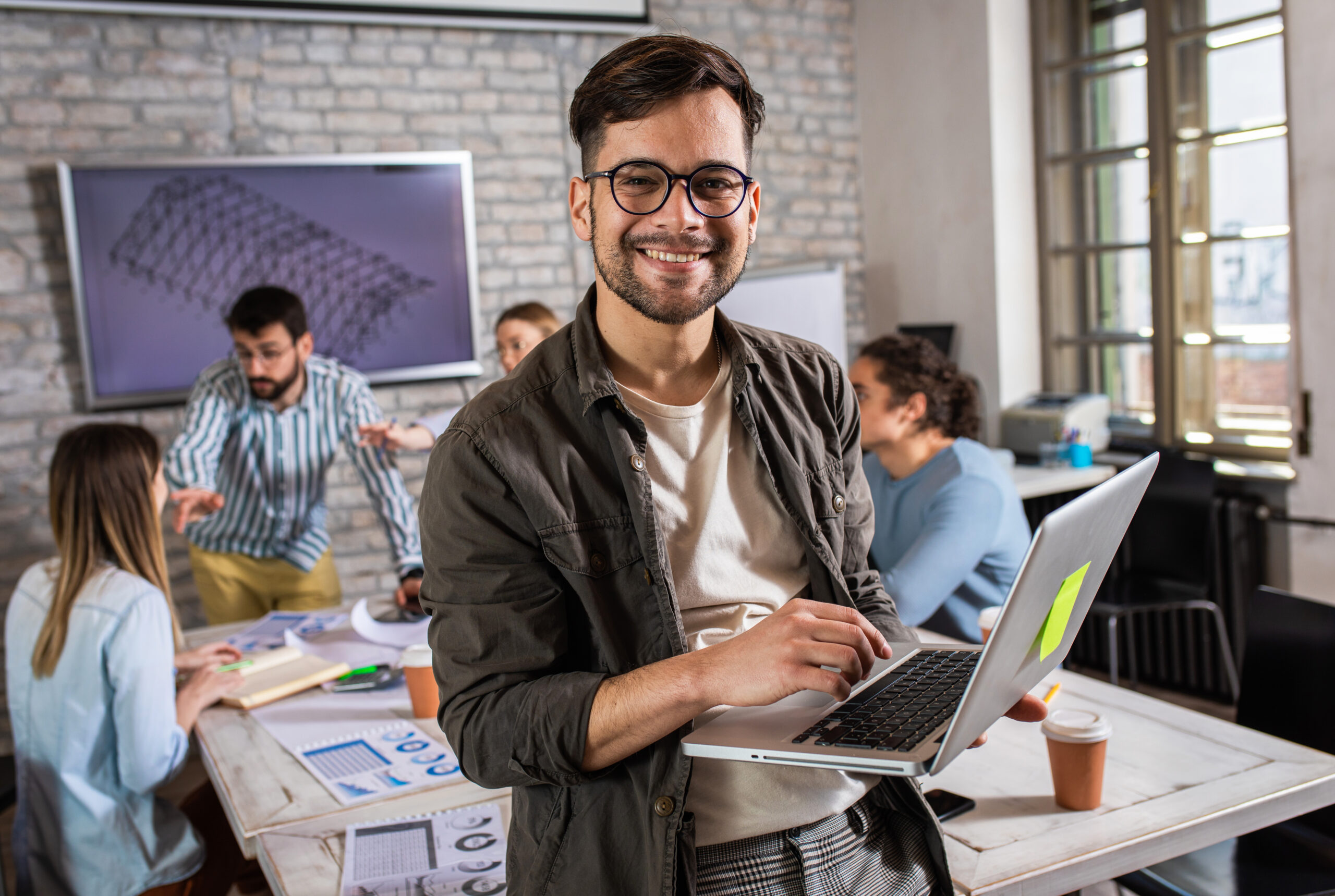 male entrepreneur with glasses holding a laptop and smiling at the camer