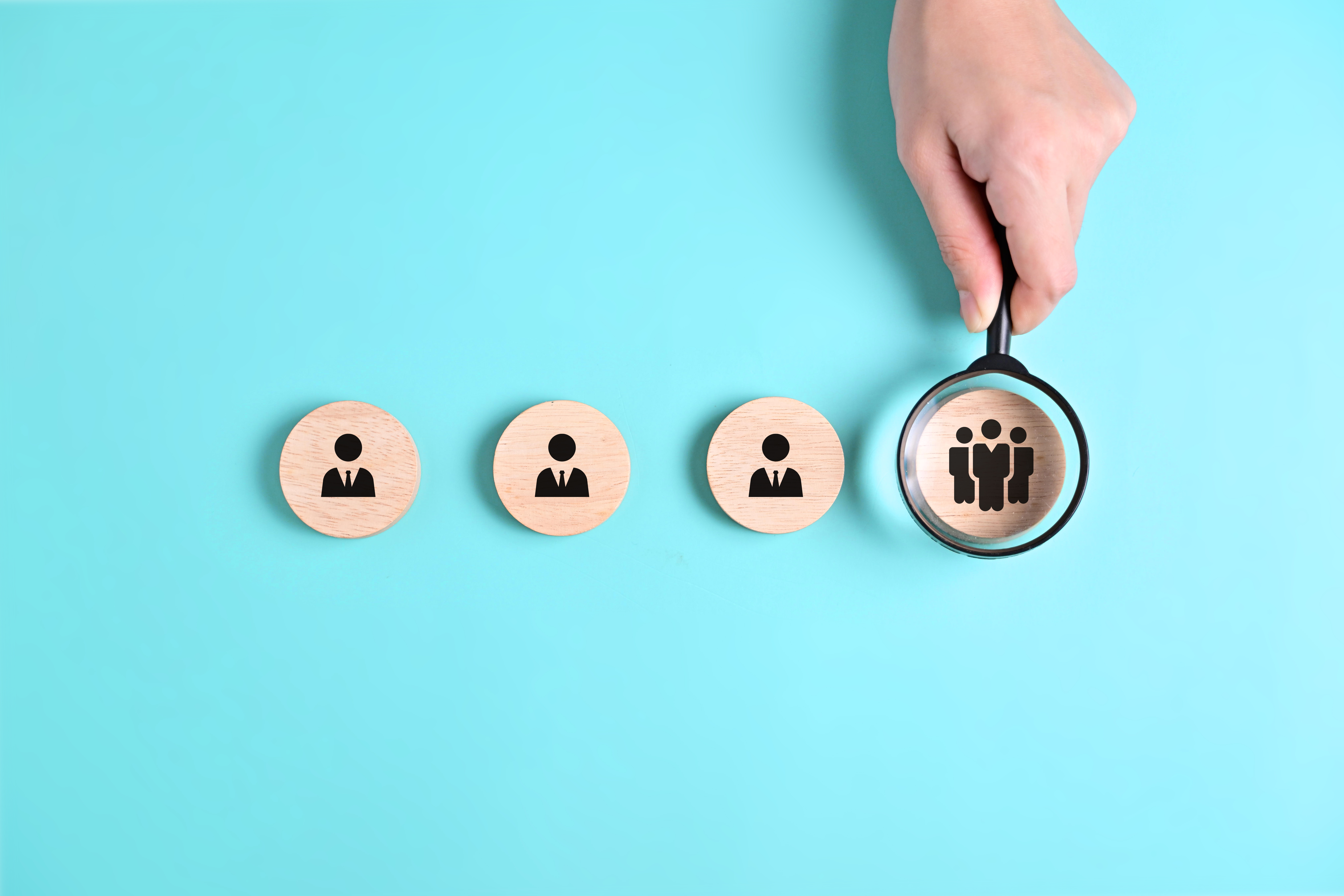 Leadership and people. Three circular wooden blocks with employees. A fourth circular block with a team icon is highlighted under a magnifying glass.