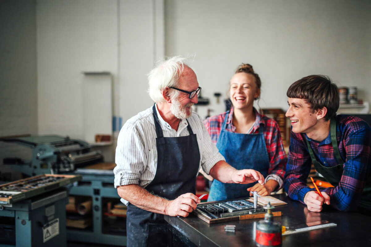 senior craftsman laughing with a young male and female learning skills through an apprenticeship