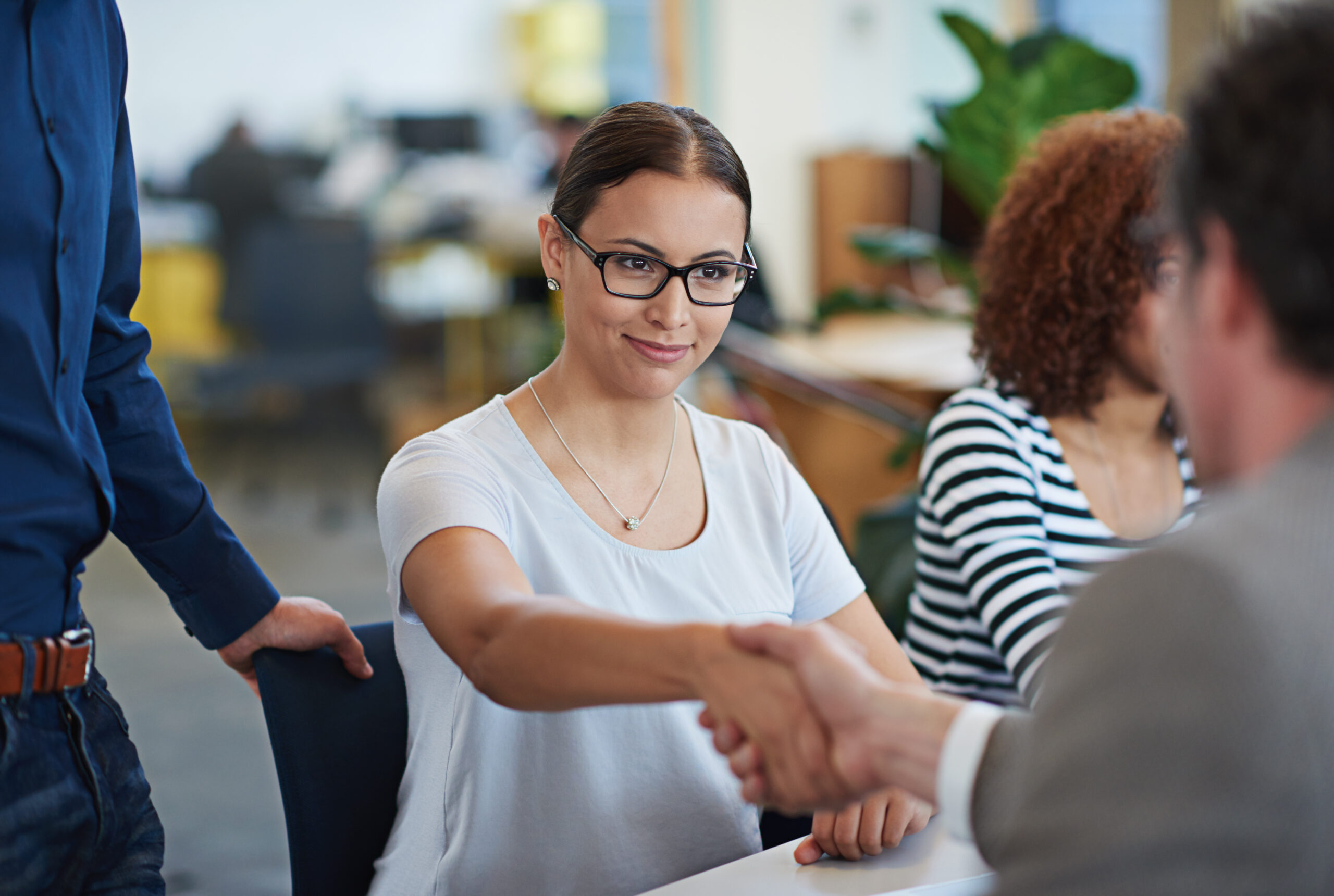 Young woman with black glasses and a white t-shirt shaking hands with a hiring manager.