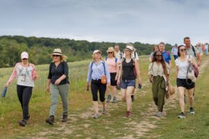 A group of mixed aged and race individuals out walking in an open field with trees behind them in the distance.