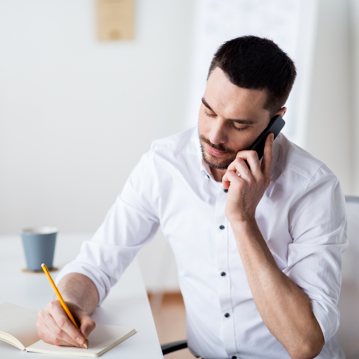 A man in a white shirt cold calling customers on a mobile phone